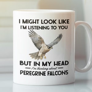 May include: White ceramic coffee mug with a black graphic of a peregrine falcon in flight. The text reads "I might look like I'm listening to you, but in my head I'm thinking about Peregrine Falcons."