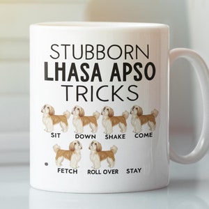 May include: White ceramic coffee mug with a black and brown illustration of a Lhasa Apso dog. The mug has the text "Stubborn Lhasa Apso Tricks" and lists various dog tricks such as "Sit", "Down", "Shake", "Come", "Fetch", "Roll Over", and "Stay".