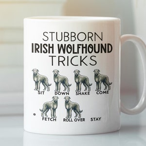 以下が含まれることがあります： 白いセラミック製のコーヒーカップに、アイルランド・ウルフハウンドの犬の黒いグラフィックと「Stubborn Irish Wolfhound Tricks」というテキストが描かれています。グラフィックは、犬がさまざまなポーズをとっている様子を示しており、それぞれのポーズの下に「Sit」、「Down」、「Shake」、「Come」、「Fetch」、「Roll Over」、「Stay」というテキストが書かれています。