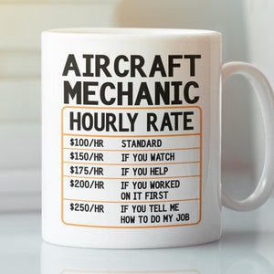 以下が含まれることがあります： 白地に黒とオレンジの模様が施されたセラミック製のマグカップ。マグカップには「Aircraft Mechanic Hourly Rate」という文字と、時間給と説明が書かれた表が描かれています。説明には、「標準」、「見ている場合」、「手伝っている場合」、「最初に作業した場合」、「作業方法を教えてくれる場合」などが含まれています。