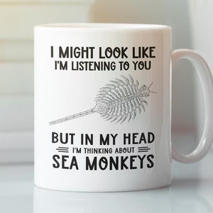 May include: White ceramic coffee mug with a black graphic that says "I might look like I'm listening to you but in my head I'm thinking about sea monkeys". The graphic also includes a black and white illustration of a sea monkey.