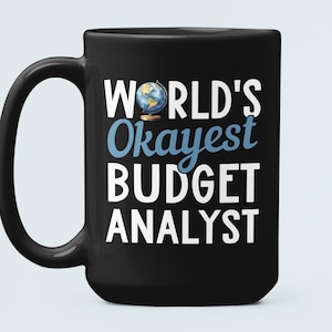 May include: Black ceramic coffee mug with a white design that reads "World's Okayest Budget Analyst". A small blue globe icon is above the word "Okayest".