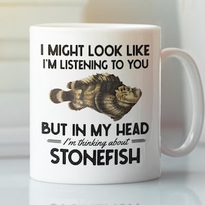 May include: White ceramic mug with a handle featuring the text "I MIGHT LOOK LIKE I'M LISTENING TO YOU BUT IN MY HEAD I'm thinking about STONEFISH." A detailed illustration of a stonefish is also on the mug.