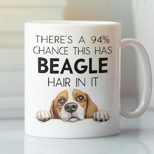 Puede incluir: Taza de cerámica blanca con el texto: "THERE'S A 94% CHANCE THIS HAS BEAGLE HAIR IN IT." La taza presenta una ilustración de un beagle de dibujos animados. La taza tiene un asa blanca y es para bebidas.