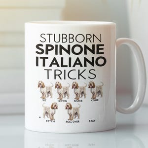 May include: White ceramic mug with the text "STUBBORN SPINONE ITALIANO TRICKS" in black. The mug features illustrations of Spinone Italiano dogs demonstrating tricks like "Sit," "Down," and "Fetch."