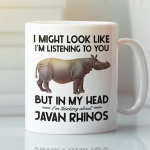 Puede incluir: Taza de cerámica blanca con una ilustración en blanco y negro de un rinoceronte de Java. La taza dice "Puedo parecer que te estoy escuchando, pero en mi cabeza estoy pensando en los rinocerontes de Java."