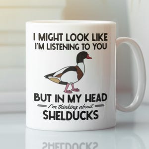 May include: White ceramic mug with a black, brown, and white shelduck illustration. The mug has the text "I MIGHT LOOK LIKE I'M LISTENING TO YOU BUT IN MY HEAD I'm thinking about SHELDUCKS."