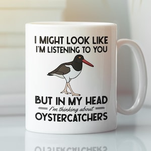May include: White ceramic mug with a black and brown bird illustration and the text "I MIGHT LOOK LIKE I'M LISTENING TO YOU BUT IN MY HEAD I'm thinking about OYSTERCATCHERS". The mug has a white handle.
