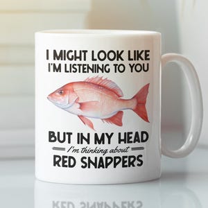 May include: White ceramic mug with a red snapper illustration and the text "I MIGHT LOOK LIKE I'M LISTENING TO YOU BUT IN MY HEAD I'm thinking about RED SNAPPERS". The mug has a white handle.