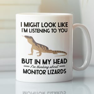 May include: White ceramic mug with a handle featuring a lizard illustration and the text "I MIGHT LOOK LIKE I'M LISTENING TO YOU BUT IN MY HEAD I'm thinking about MONITOR LIZARDS". The mug is a humorous gift for reptile enthusiasts.