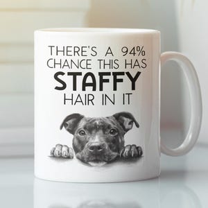 Könnte beinhalten: Weiße Keramiktasse mit einer schwarz-weißen Grafik eines Staffordshire Bull Terrier. Die Tasse trägt den schwarzen Text "THERE'S A 94% CHANCE THIS HAS STAFFY HAIR IN IT". Die Tasse hat einen weißen Henkel.