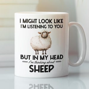 May include: White ceramic mug with a humorous message and a sheep illustration. The text reads "I MIGHT LOOK LIKE I'M LISTENING TO YOU BUT IN MY HEAD I'm thinking about SHEEP". The mug has a white handle.