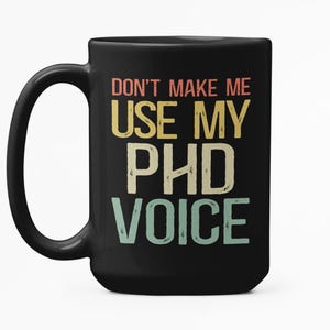 May include: Black ceramic mug with the text "DON'T MAKE ME USE MY PHD VOICE" in a retro colour scheme. The mug has a large handle and a glossy finish. A humorous gift for a graduate or professor.