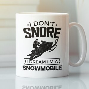 May include: White ceramic mug with a black graphic that says "I don't snore I dream I'm a snowmobile". The graphic also includes a silhouette of a person riding a snowmobile.