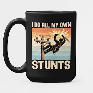 May include: Black ceramic mug featuring a graphic of a lineman on a power line. The text "I DO ALL MY OWN STUNTS" is displayed in white. The background has a sunset colour scheme with orange, blue, and beige.