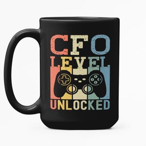 Puede incluir: Taza de cerámica negra con el texto "CFO LEVEL UNLOCKED" en una fuente retro, con un gráfico de mando. El texto es en rojo, naranja, amarillo y azul. La taza tiene un asa grande.