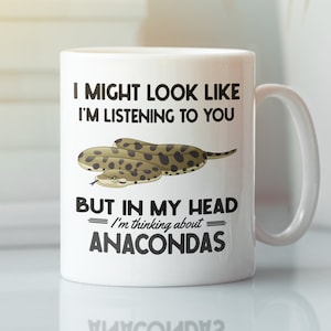 Könnte beinhalten: Eine weiße Keramik-Kaffeetasse mit einer schwarzen und braunen Schlangenillustration und dem Text "I might look like I'm listening to you but in my head I'm thinking about ANACONDAS".