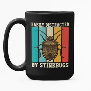 Könnte beinhalten: Schwarze Keramik-Tasse mit dem weißen Text "EASILY DISTRACTED BY STINKBUGS". Die Tasse zeigt eine Grafik einer Stinkwanze über einem Retro-Hintergrund aus vertikalen Streifen in Türkis, Blau, Beige, Rot und Gelb.