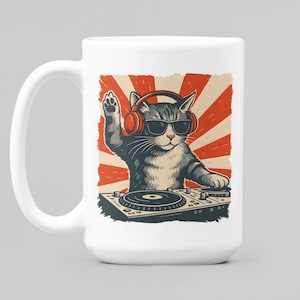 May include: White ceramic mug featuring a cartoon cat DJ wearing sunglasses and headphones, with a red and orange burst design in the background. The cat is positioned behind a turntable, with one paw raised.