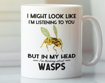May include: White ceramic mug with a humorous design. The mug features a yellow and black wasp illustration and the text: "I MIGHT LOOK LIKE I'M LISTENING TO YOU BUT IN MY HEAD I'm thinking about WASPS."