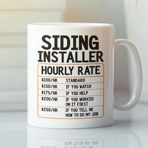 May include: White ceramic mug with a black and orange design. The mug reads "Siding Installer Hourly Rate" with a table listing different hourly rates and descriptions. The descriptions include "Standard", "If you watch", "If you help", "If you worked on it first", and "If you tell me how to do my job".