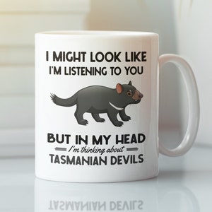 Puede incluir: Taza de cerámica blanca con una ilustración en blanco y negro de un demonio de Tasmania. La taza tiene el texto "Puedo parecer que te escucho, pero en mi cabeza estoy pensando en demonios de Tasmania."