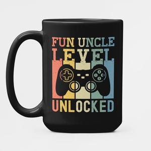 May include: A black ceramic mug featuring a graphic print with the text FUN UNCLE LEVEL UNLOCKED. The design includes a stylized game controller silhouette centered over vertical stripes in muted red, yellow, and blue tones.