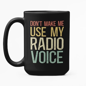 May include: Black ceramic coffee mug with a large handle. The mug features the text "DON'T MAKE ME USE MY RADIO VOICE" in a retro, multi-colored font. The mug is designed for hot or cold beverages.