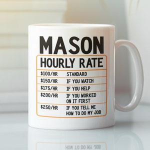 May include: White ceramic mug with the word "MASON" in bold black letters. Below, "HOURLY RATE" is printed, followed by a list of hourly rates and corresponding phrases. The mug has a curved handle and is set against a blurred background.