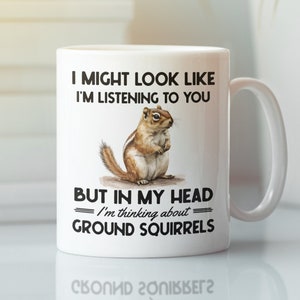 May include: White ceramic mug with a black and white graphic of a squirrel. The text on the mug reads "I might look like I'm listening to you but in my head I'm thinking about ground squirrels."