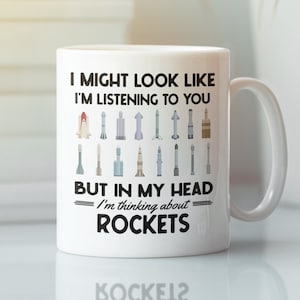 May include: White ceramic coffee mug with a black graphic that reads "I might look like I'm listening to you, but in my head I'm thinking about rockets". The graphic includes a variety of rockets and spacecrafts.