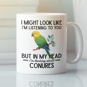 Könnte beinhalten: Eine weiße Keramiktasse mit einer schwarz-weißen Grafik eines grün-gelben Conure-Papageis. Der Text auf der Tasse lautet "Ich mag aussehen, als würde ich zuhören, aber in meinem Kopf denke ich an Conures."