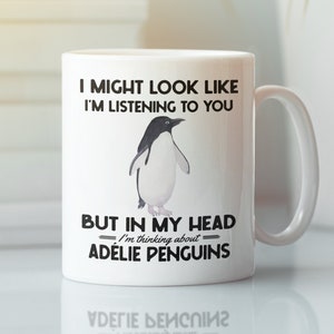 Pode incluir: Caneca de cerâmica branca com uma ilustração em preto e branco de um pinguim. A caneca tem o texto "Posso parecer que estou te ouvindo, mas na minha cabeça estou pensando em pinguins-de-adélia."