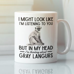 May include: White ceramic mug with a black and white image of a gray langur monkey. The mug has the text "I might look like I'm listening to you, but in my head I'm thinking about gray langurs."