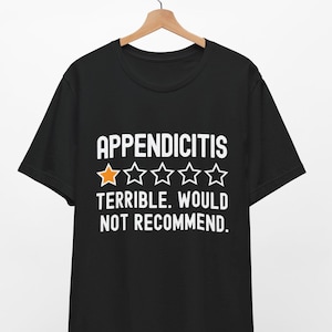 Könnte beinhalten: Schwarzes T-Shirt mit weißem Text, der "Appendizitis" lautet und eine ein-Sterne-Bewertung erhält. Der Text unter der Bewertung lautet "Schrecklich. Nicht zu empfehlen."