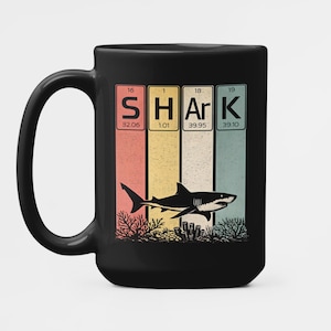 Peut inclure: Mug en céramique noire avec un motif de requin. Le mot "SHARK" est épelé à l'aide d'éléments du tableau périodique. Le motif comprend une silhouette de requin noir et du corail sur un fond rayé orange, jaune et turquoise.