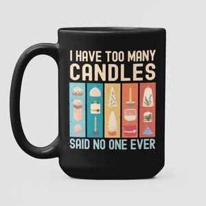 Könnte beinhalten: Schwarze Kaffeetasse mit einer weißen Grafik, auf der steht "Ich habe zu viele Kerzen, das hat noch nie jemand gesagt". Die Grafik zeigt ein Vintage-Design mit einem Regenbogen aus Farben und Illustrationen verschiedener Kerzen.