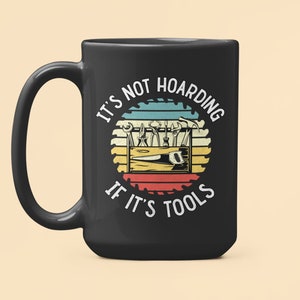 May include: Black coffee mug with a white graphic of a toolbox with tools and the text "It's not hoarding if it's tools" in a retro style.
