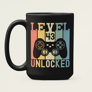 May include: Black coffee mug with a retro-style design featuring a video game controller and the text "LEVEL 43 UNLOCKED".