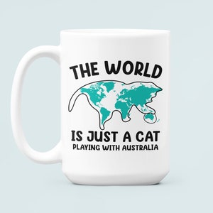 May include: White ceramic mug with a large handle. The mug features the text "THE WORLD IS JUST A CAT PLAYING WITH AUSTRALIA" in black and a teal cat-shaped world map design.