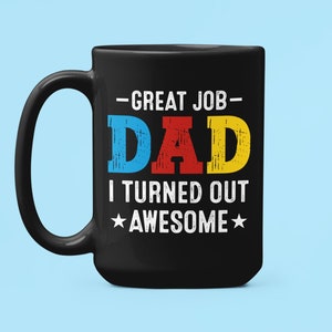 May include: Black coffee mug with a white design that says "Great Job Dad I Turned Out Awesome" with the word "Dad" in colorful letters.