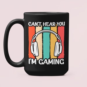 May include: Black coffee mug with a retro-style design featuring a pair of headphones and the text "Can't hear you I'm gaming".