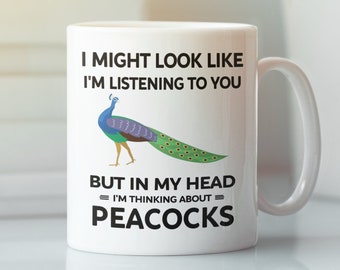 May include: White ceramic mug with a black and white graphic of a peacock. The text on the mug reads "I might look like I'm listening to you, but in my head I'm thinking about peacocks."