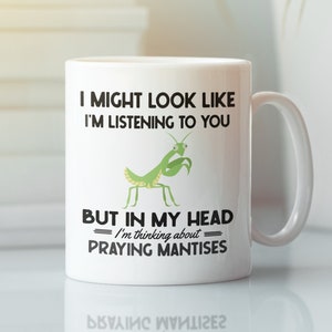May include: White ceramic mug with a black and white graphic of a praying mantis. The text on the mug reads "I might look like I'm listening to you but in my head I'm thinking about praying mantises."