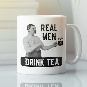 May include: White ceramic mug with a black and white image of a man holding a teacup. The text "REAL MEN DRINK TEA" is printed on the mug.