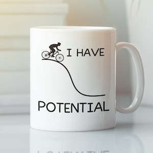 May include: White ceramic mug with a black silhouette of a person riding a bicycle up a hill. The text "I have potential" is printed on the mug.
