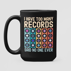 Può includere: Tazza da caffè nera con una grafica bianca che dice "Ho troppi dischi, nessuno l'ha mai detto". La grafica presenta anche una pila di dischi in vinile colorati.