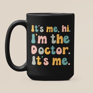 May include: Black coffee mug with the text "It's me, hi. I'm the doctor. It's me." in colorful, playful lettering.
