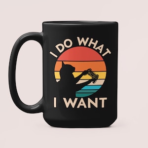May include: Black coffee mug with a white graphic of a cat holding a video game controller. The graphic is set against a sunset background with the text "I do what I want".