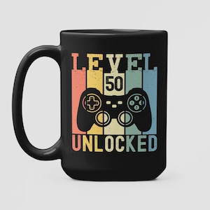 May include: Black coffee mug with a retro-style graphic of a video game controller and the text "LEVEL 50 UNLOCKED".